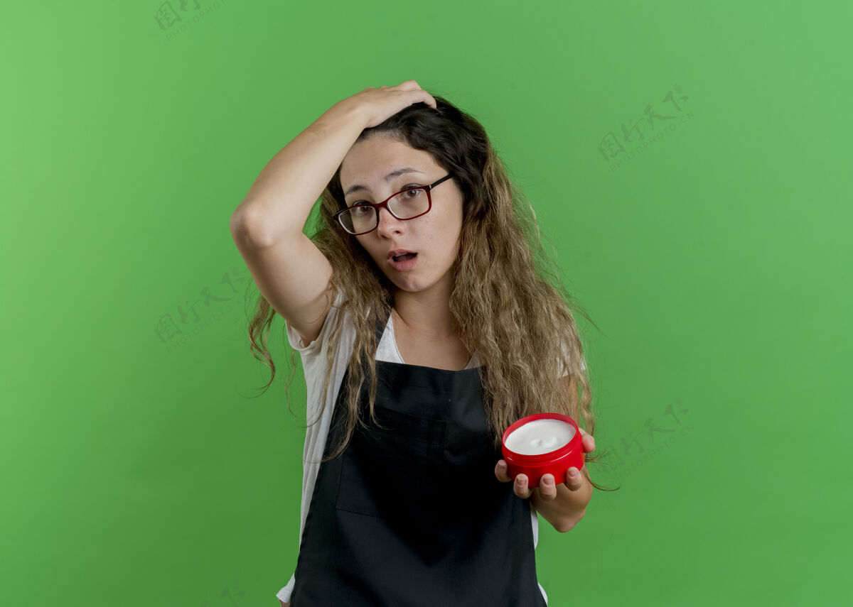 拿着年轻的专业美发师女士围着围裙拿着一罐发膏 用手误按在头上罐子头发女人