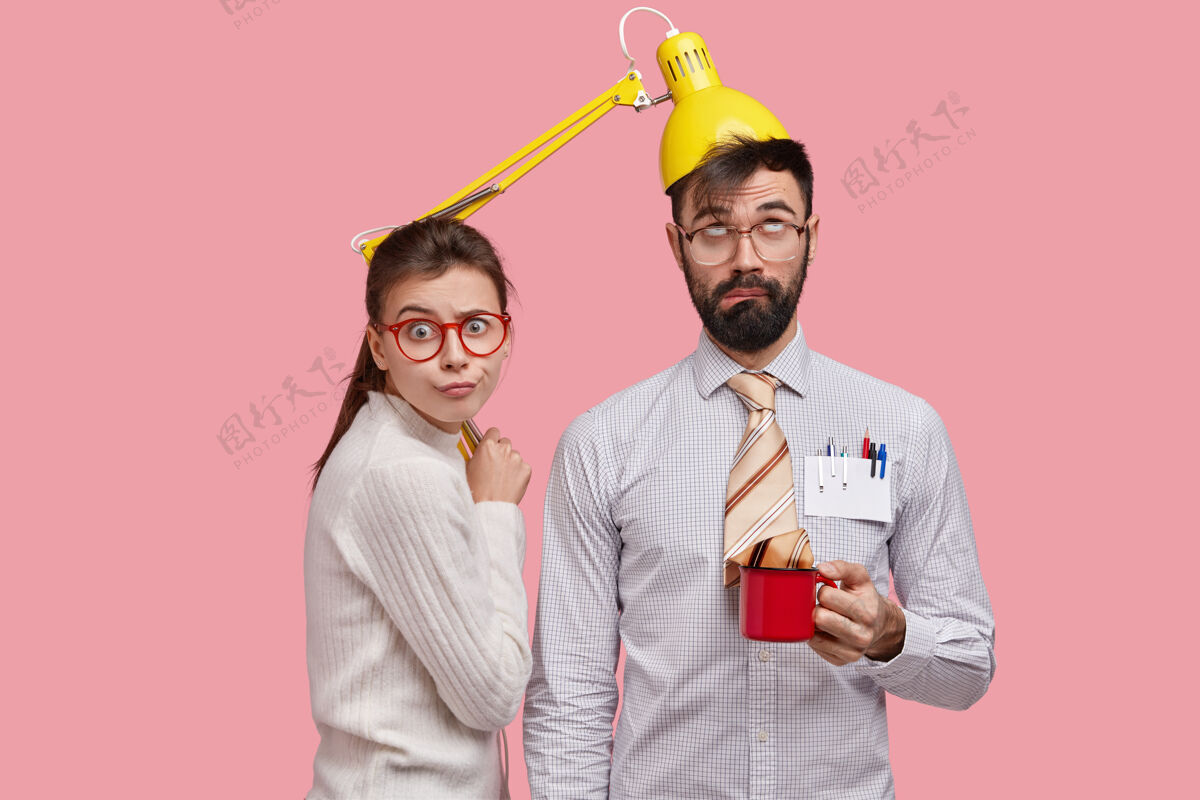 合作照片中滑稽的胡须男青年头上有台灯 扎着一杯茶 身着正装 他的女搭档站在旁边书呆子呆子杯子