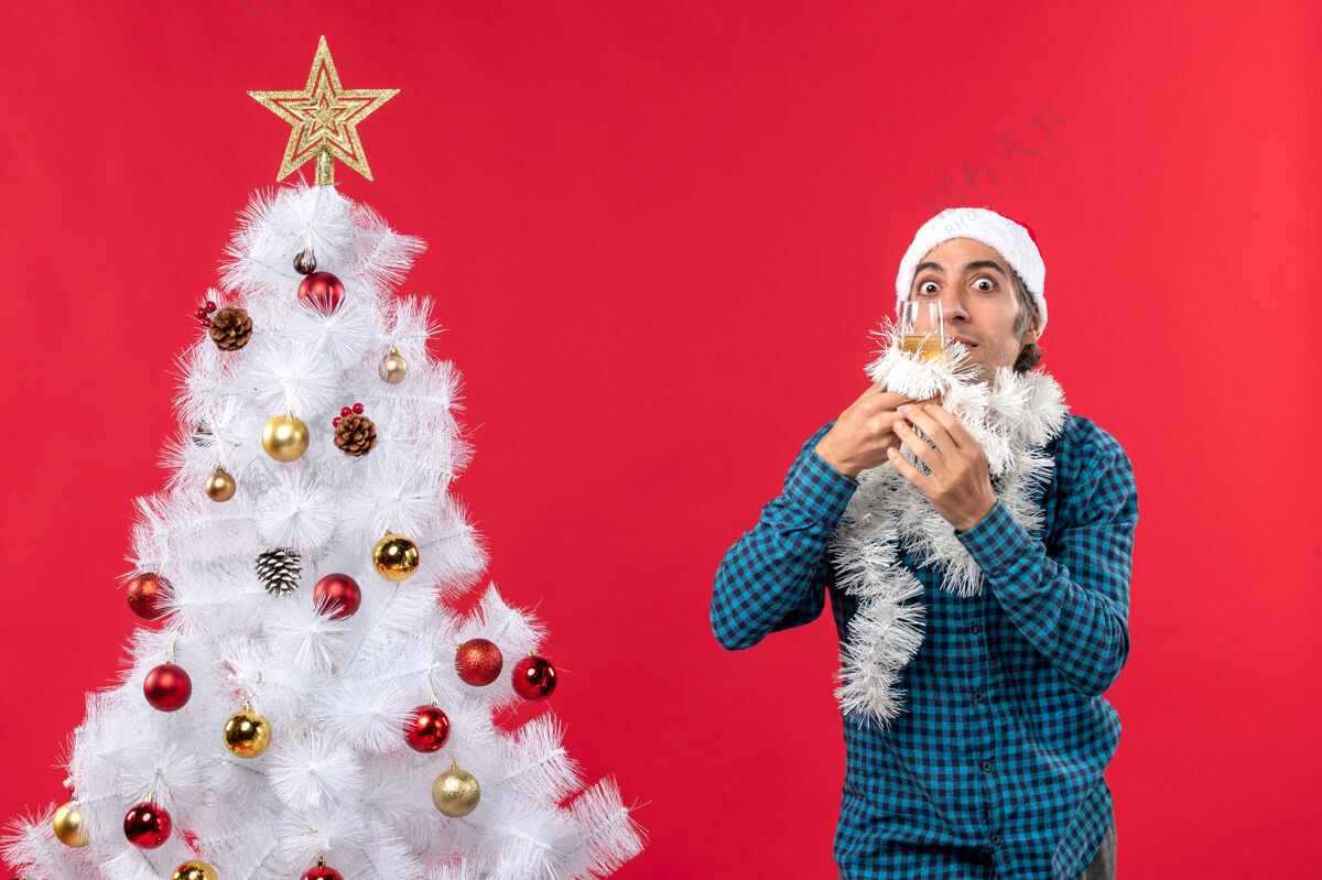 葡萄酒圣诞气氛和戴圣诞老人帽的年轻人 举起一杯葡萄酒 在圣诞树旁为自己欢呼新年快乐圣诞树