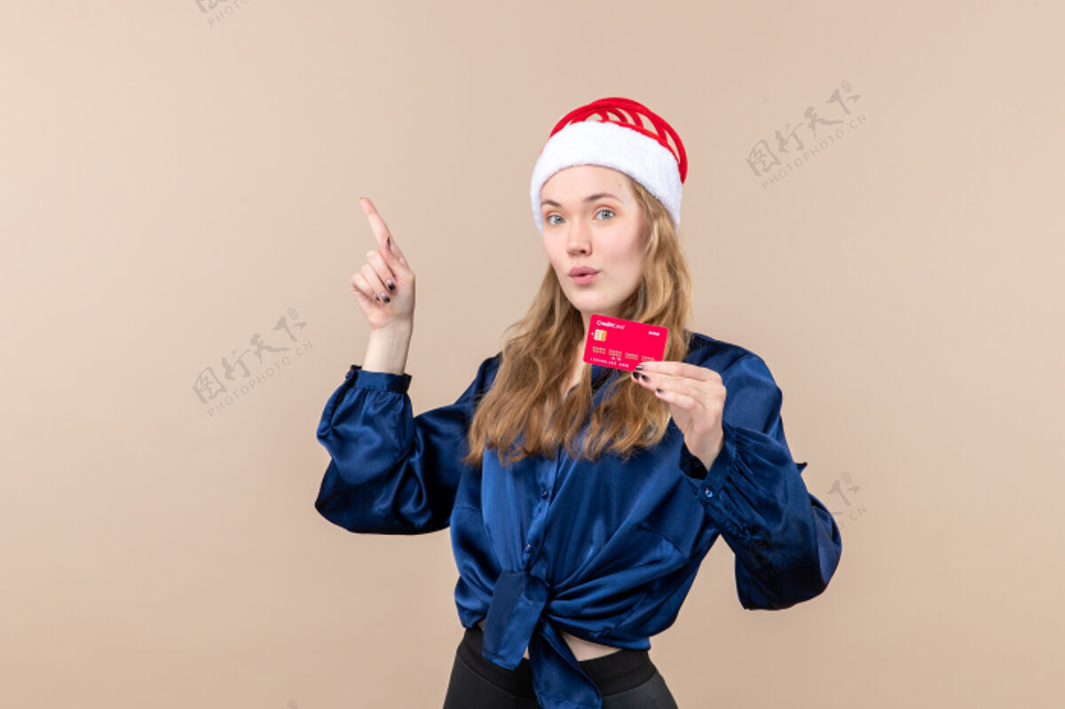 成人正面图年轻女性手持红色银行卡 背景为粉色假日照片新年圣诞钱情肖像帽子情感