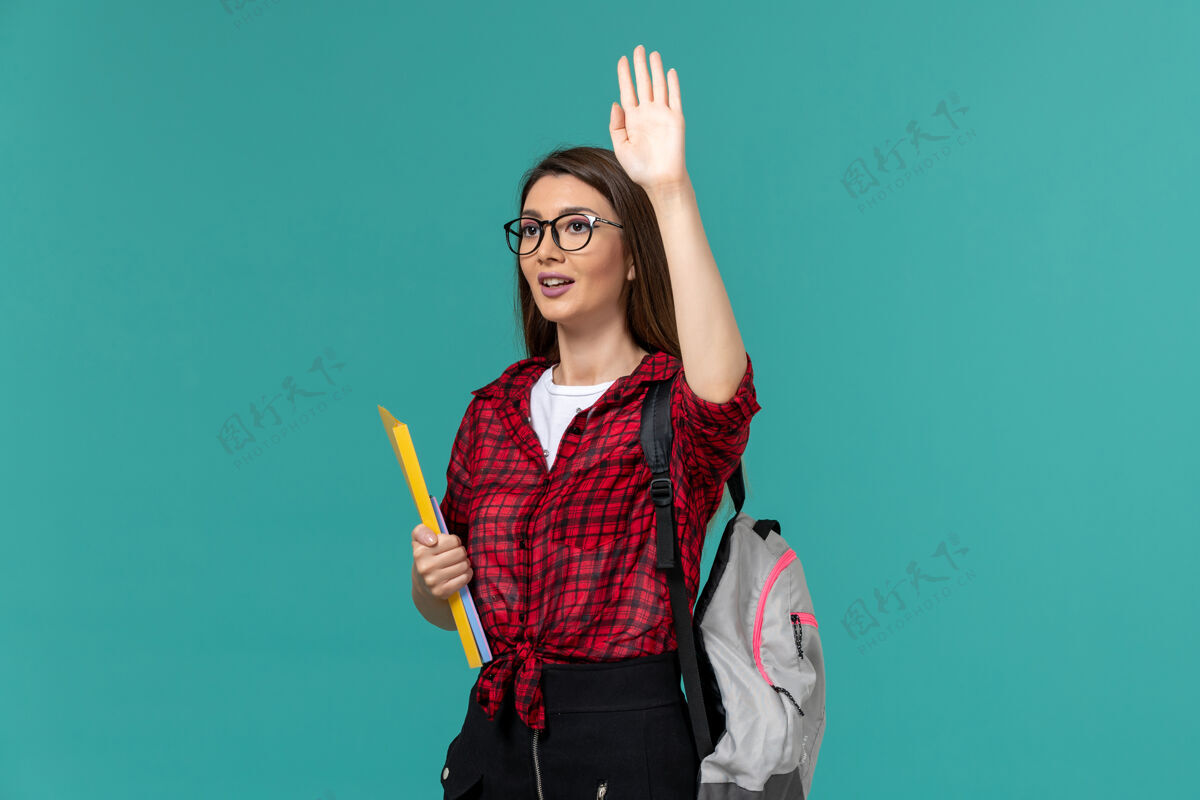 人女学生背着书包 手里拿着文件 手举在蓝色的墙上正面教训人