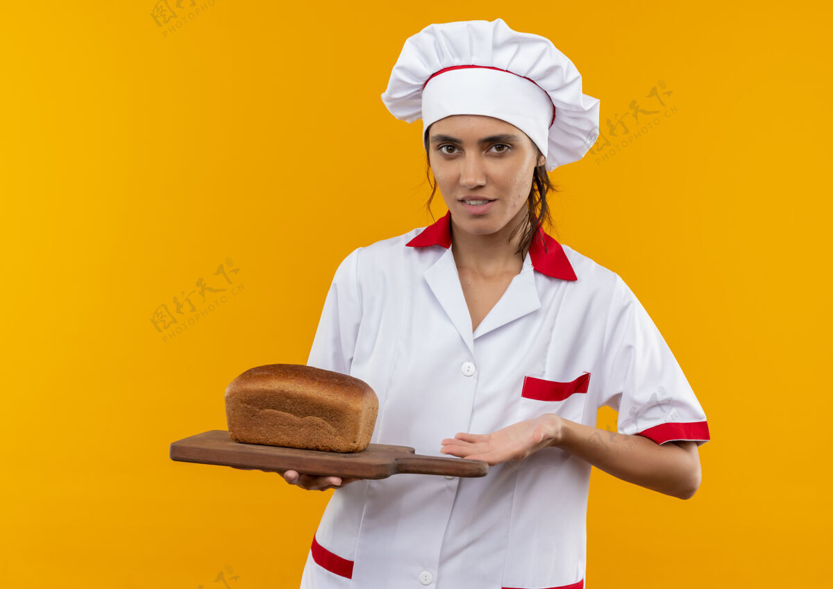 拿着年轻的女厨师穿着厨师制服 拿着面包放在隔离的黄色墙壁上的砧板上 还有复印空间厨师厨师穿