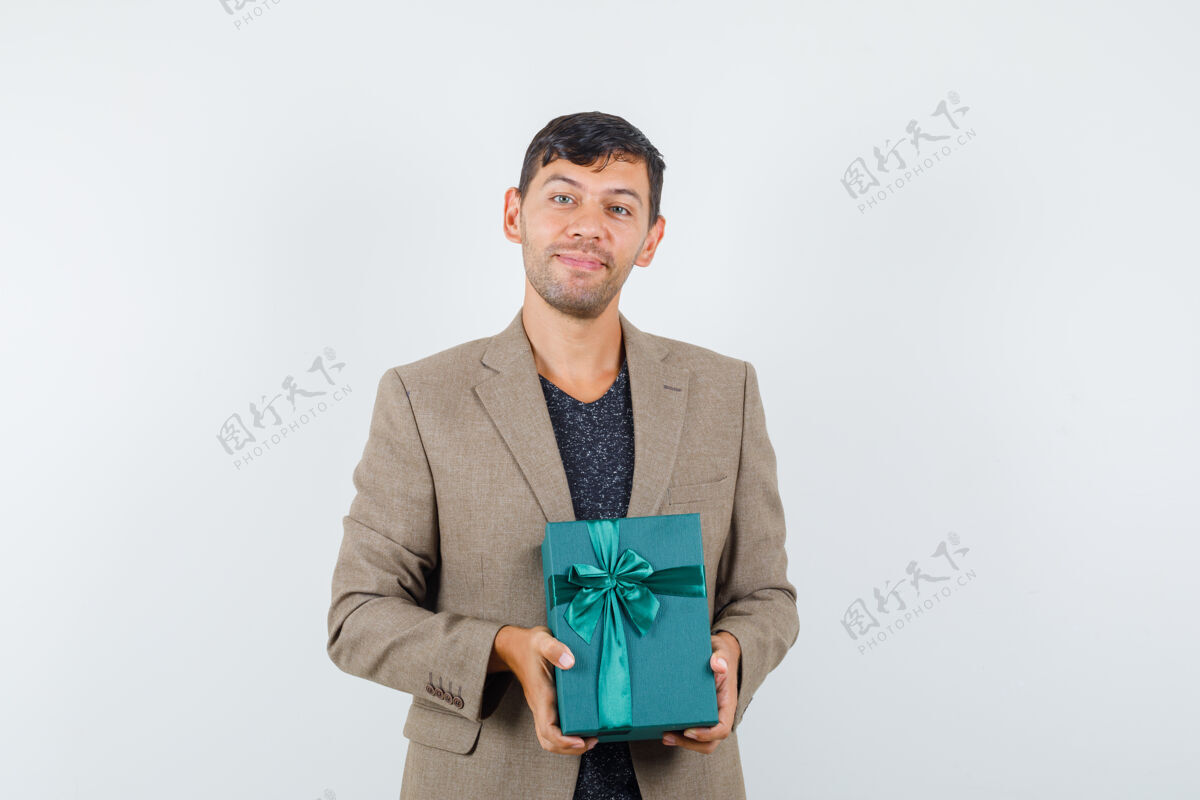 帅气年轻的男人拿着蓝色的礼盒 穿着灰褐色的夹克 看上去很高兴正面图站着肖像夹克