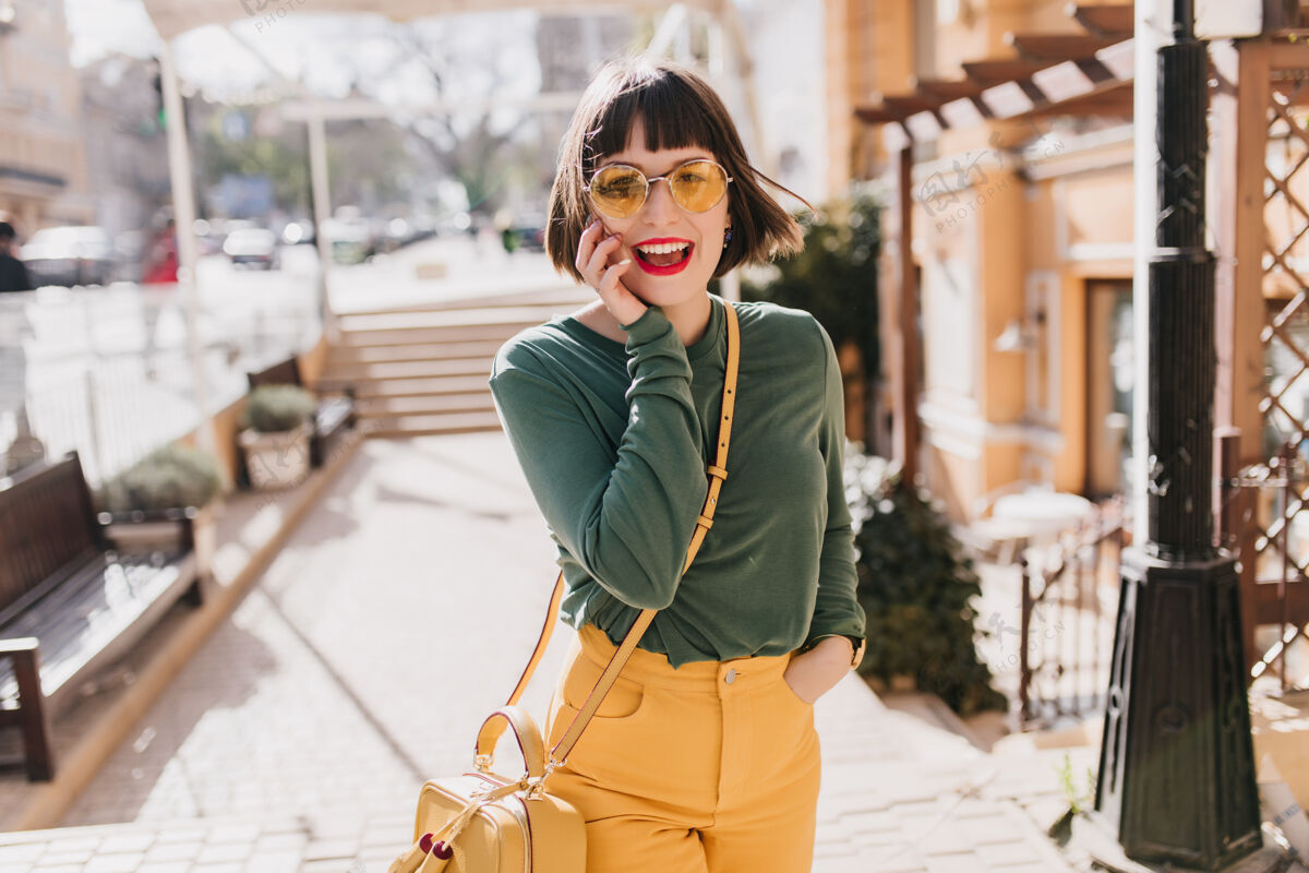 情感优雅的白种女孩戴着太阳镜在城市里表达春天的快乐可爱的女模特带着黄色手提包笑着的户外照片表情华丽时尚