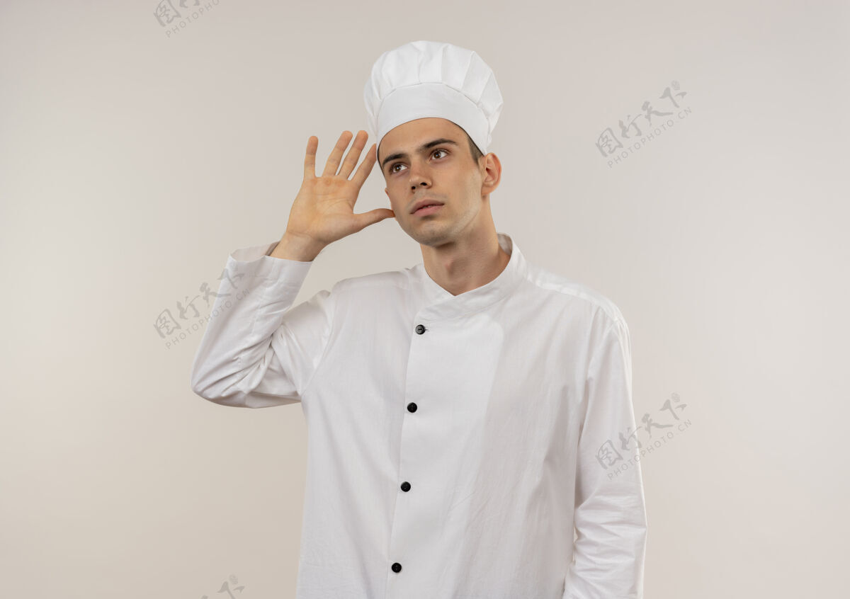 看仰望着身穿厨师制服的年轻男厨师 在隔离的白色墙壁上展示着倾听的手势 还有复制空间厨师年轻手势