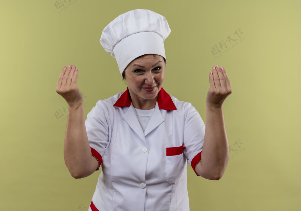 手势身着厨师制服的中年女厨师在与世隔绝的绿色墙壁上展示小费手势中年看高兴