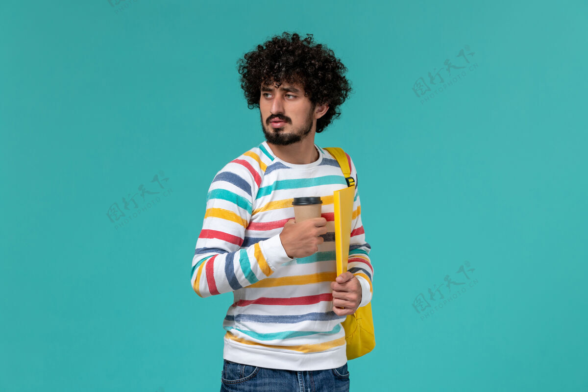 教训穿着条纹衬衫 背着黄色背包 拿着文件和咖啡的男学生在蓝色墙上的正视图条纹快乐学校
