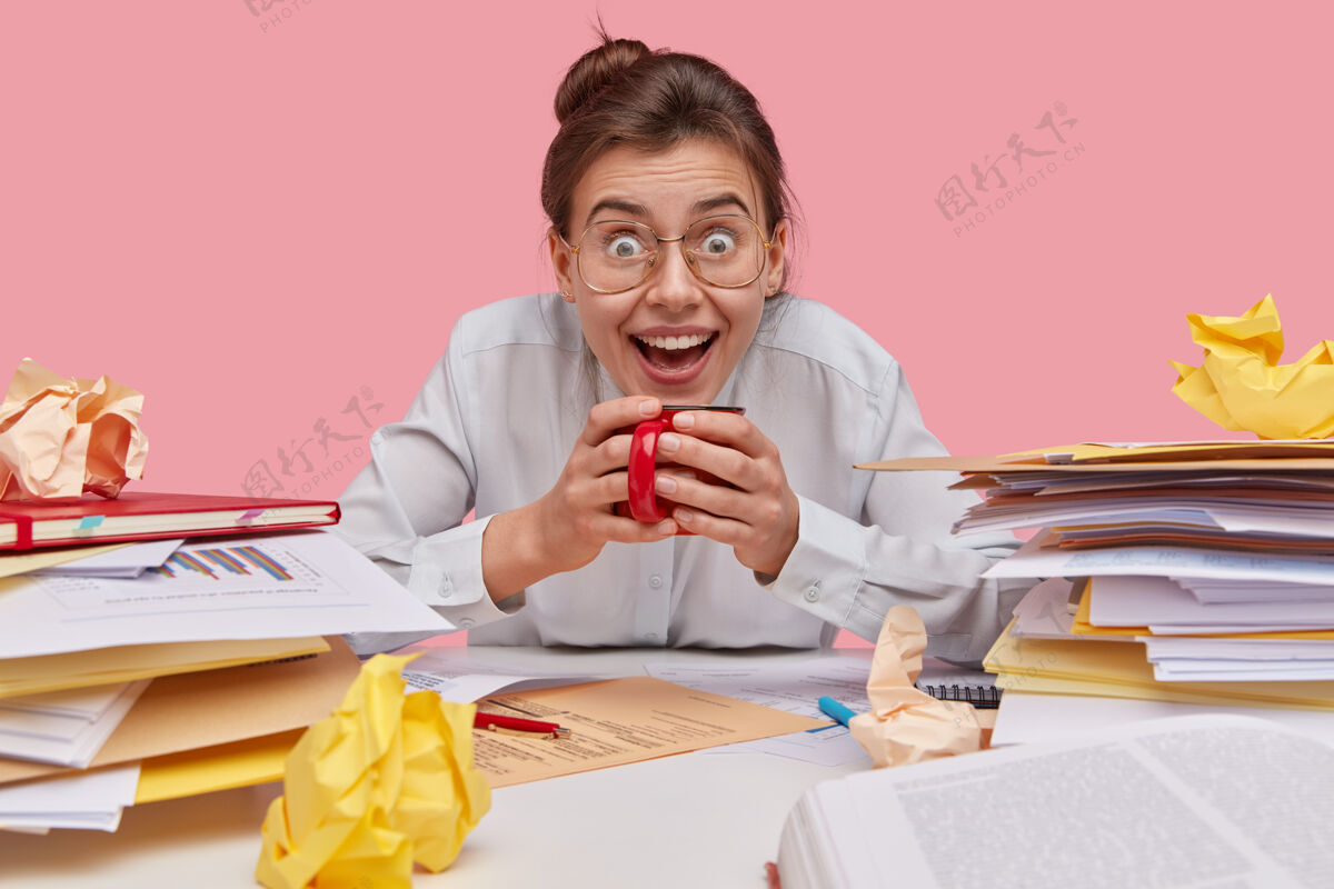 发髻一位年轻的女大学生戴着眼镜 喝着茶 穿着白衬衫 兴高采烈 忙着工作凝视饮料日记