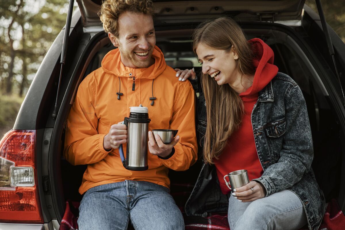 水平笑脸夫妇在汽车后备箱里享用热饮料的前视图旅行饮料冒险