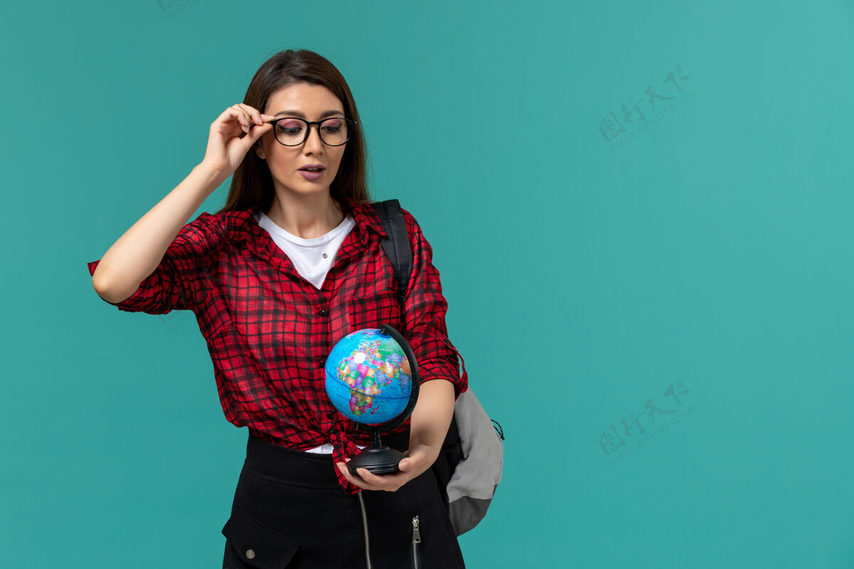 穿女学生背着背包 手持浅蓝色墙上的小地球仪的正面图前课游戏