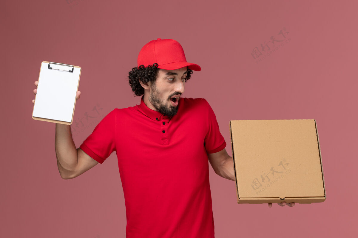 成人正面图：身穿红色衬衫和披风的男性快递员在粉色墙上拿着快递食品盒和记事本人粉色送货