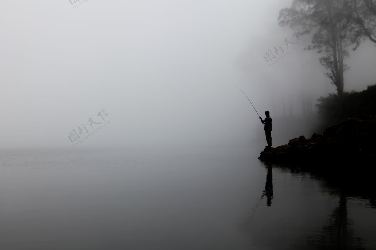捕获一个男人在浓雾笼罩的湖面上钓鱼的剪影水爱好雾