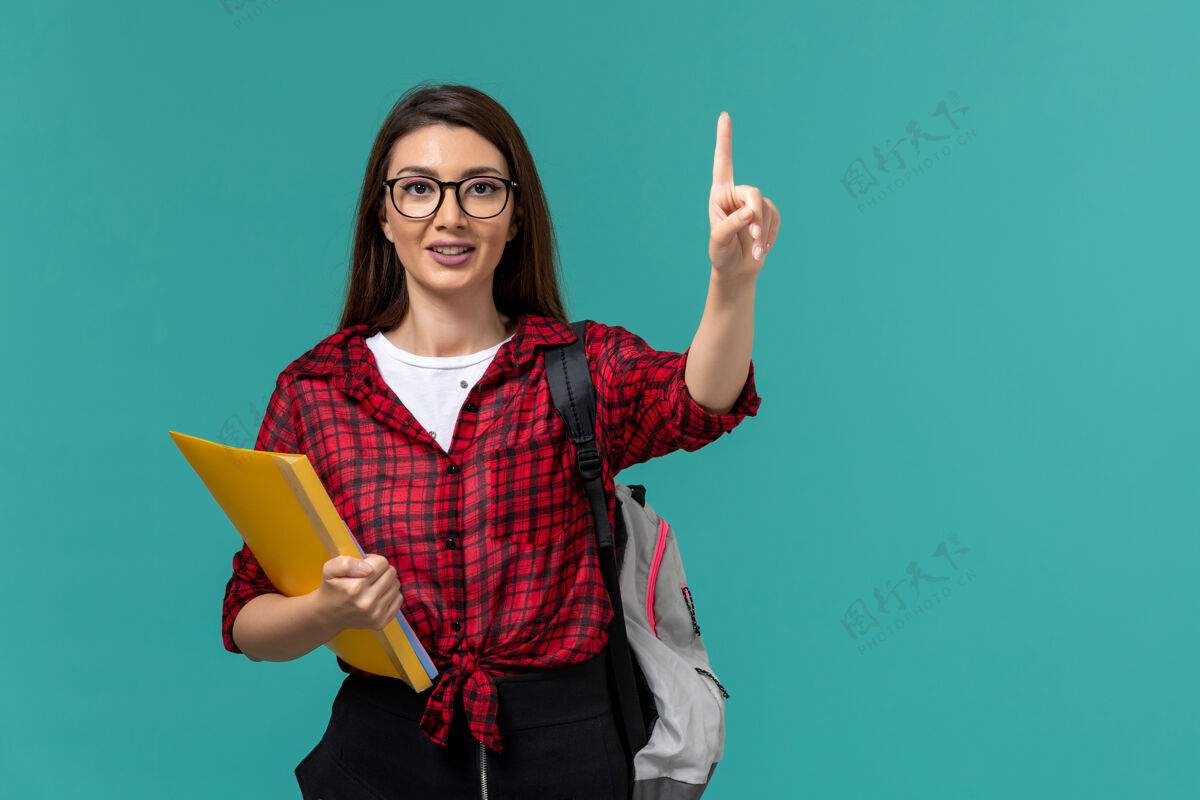 保持女学生背着背包 拿着文件微笑着站在浅蓝色的墙上文件画像大学