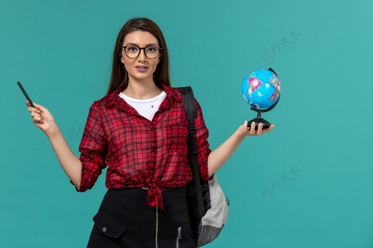 穿女学生背着背包 拿着小地球仪和钢笔 站在浅蓝色的墙上肖像大学女学生