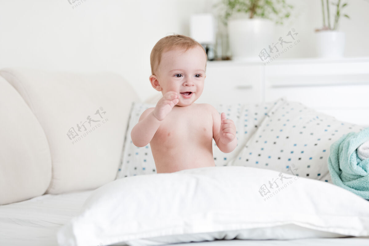 乐趣快乐的裸体男婴在床上玩枕头的画像肖像坐着有趣